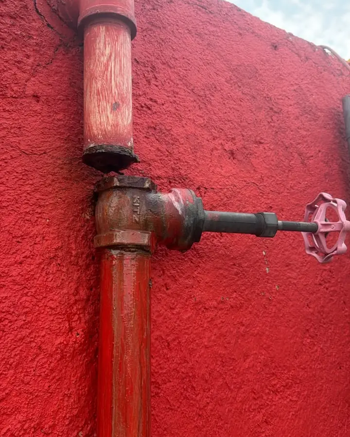 Tubería de agua con llave de paso en un muro exterior pintado de rojo