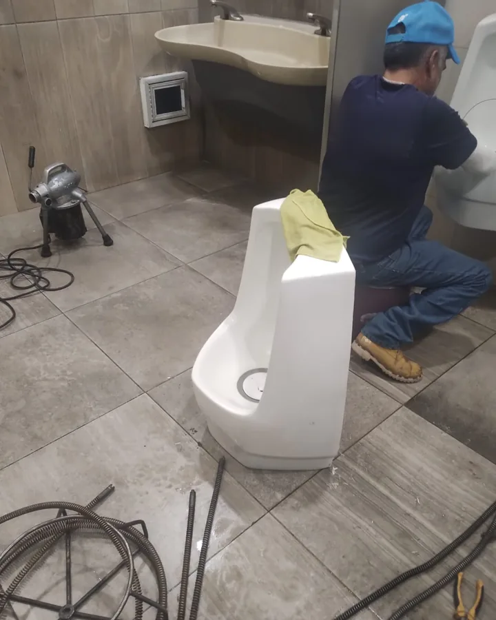 Plomero destapando un mingitorio con sonda eléctrica en un baño comercial