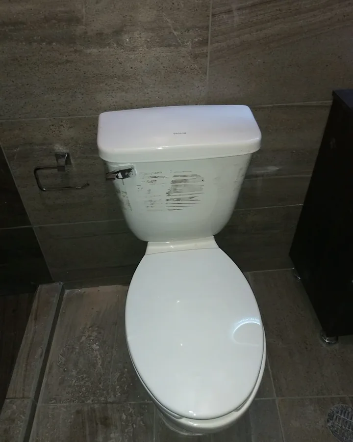 WC blanco nuevo instalado en un baño con azulejo gris
