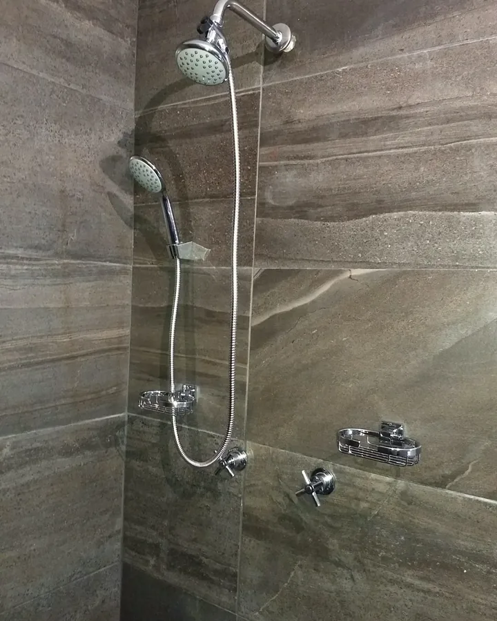 Regadera con teléfono y mezcladoras cromadas instaladas en un baño con azulejo gris
