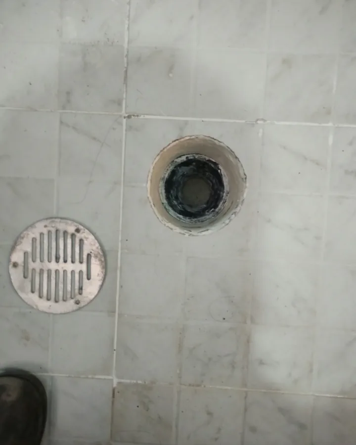 Desagüe de regadera con su rejilla a un lado en un piso de mármol