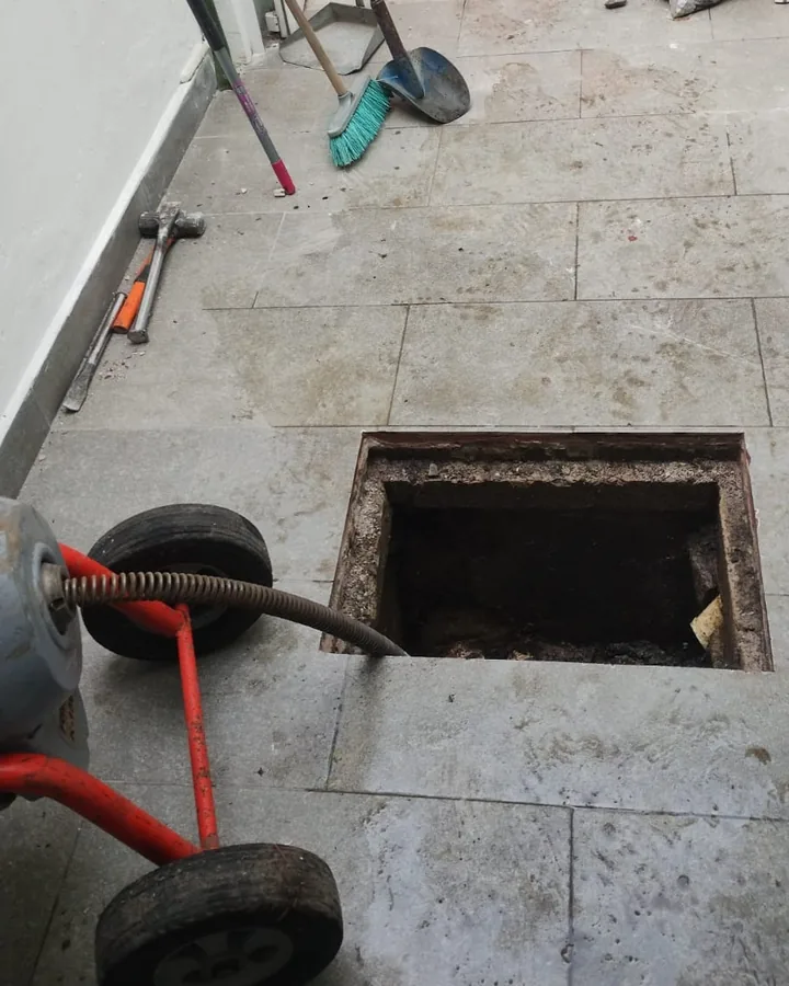 Máquina de sonda junto a un registro de drenaje abierto en un patio con herramientas