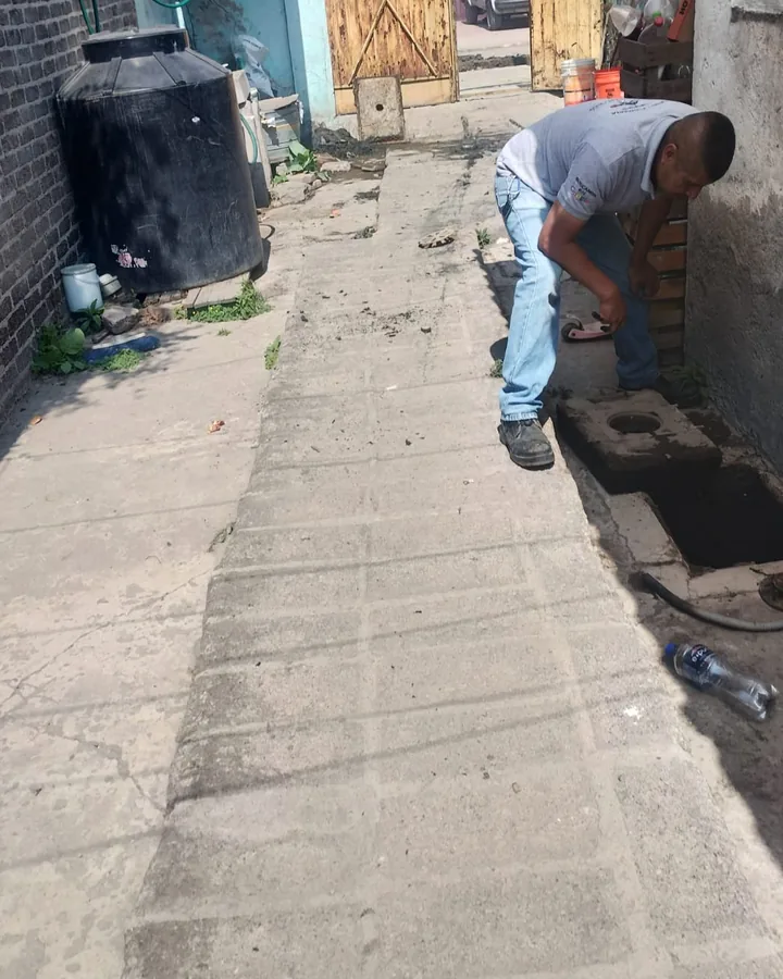 Plomero revisando un registro de drenaje en un pasillo junto a un tinaco