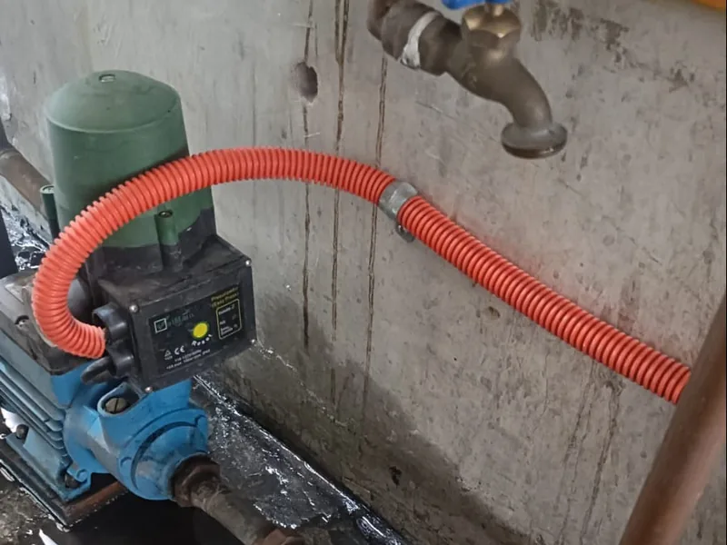 Bomba presurizadora con control de presión y manguera corrugada instalada junto a una llave